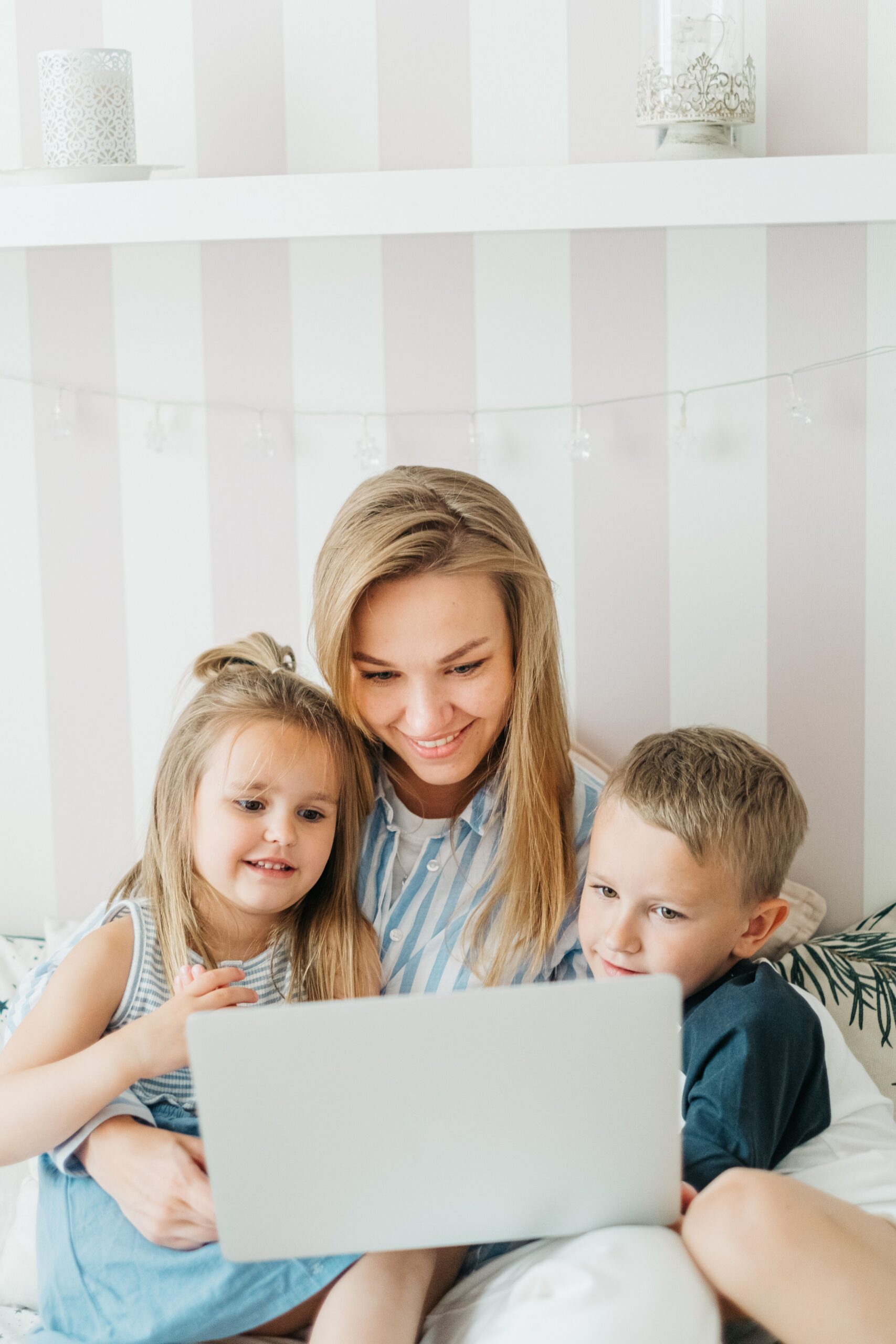 ESA School Choice Smiling mother and two children enjoying time together while watching something on a laptop in a cozy bedroom.